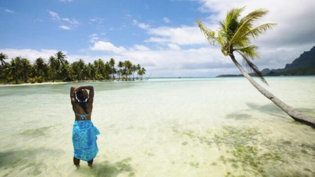 Женщина стоит в мелкой лагуне, любуясь тропическим видом на Бор Бор.