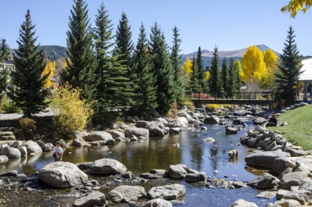 Брекенридж, Колорадо, США - 12 октября 2015 года: Жители Брекенриджа наслаждаются великолепным осенним днем у реки Блю в площади и на набережной Блю, расположенной в городе Брекенридж, Колорадо, который был основан в ноябре 1859 года генералом Джорджем Е. Спенсером. Река Блю течет через парк на набережной, созданный как проект по восстановлению города Брекенридж. Исторический город Брекенридж - самый населенный муниципалитет округа Саммит, Колорадо, США. Город расположен у подножия горного хребта Тенмайл. Летние месяцы в Брекенридже привлекают любителей активного отдыха с маршрутами для пеших прогулок, дикими цветами, ловлей рыбы на реке Блю, горным велосипедным спортом, ближайшим озером Диллон для прогулок на лодке, рафтингом, альпийскими горками и несколькими магазинами вдоль главной улицы.