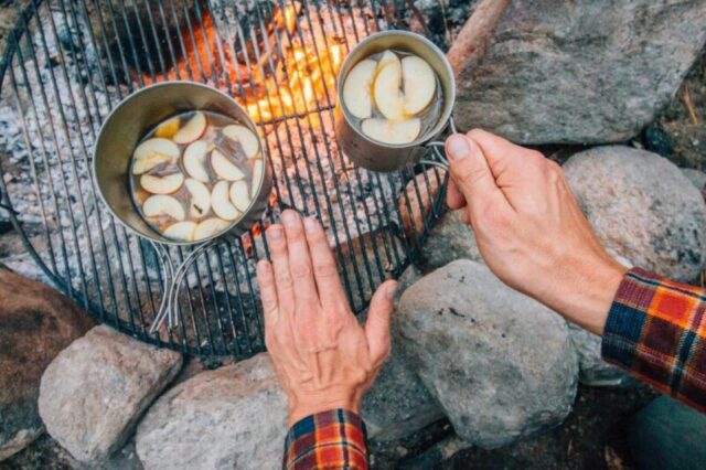 Майкл сидит у костра с бокалом сидра в руках и греет ими свои ладони