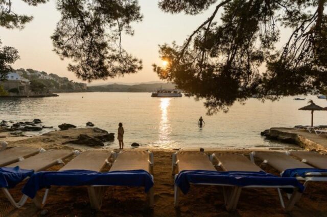 МАЙОРКА, ИСПАНИЯ, АВГУСТ 2024..Тихий пляж на закате с шезлонгами и круизным кораблем вдалеке на Майорке..Фелипе Сантибальес для нашей редакции. BIT 2025