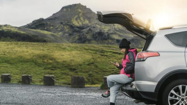 Женщина-туристка путешествует на внедорожнике по Исландии. Путешественник паркует машину и наслаждается красивыми пейзажами горного ландшафта на заднем плане. Открытие и исследование.