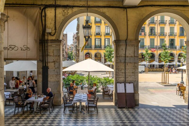 22 июня 2018 года: Люди, сидящие в ресторане на площади Независимости в центре Жироны.  1130729384 здание, кафе, каталония, каталунья, коста брава, испания, европа, жерона, жирона, исторический, на улице, пласа де ла индепендэнс, ресторан, рестораны, испания, площадь, улица, туризм, турист